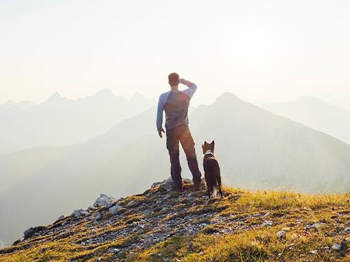 En mann står med en hund på et fjell